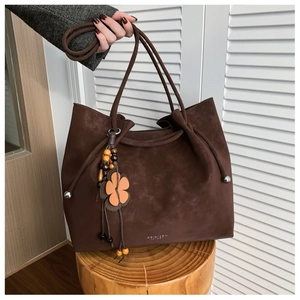 Detail of dark brown suede tote bag featuring a floral wooden bead tassel charm