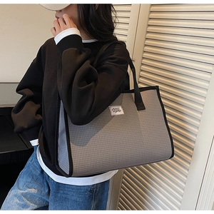 Close-up of gray plaid tote bag featuring a black woven strap and brand label
