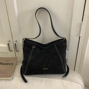 Détail du sac à bandoulière en daim noir avec surpiqûres blanches et logo doré