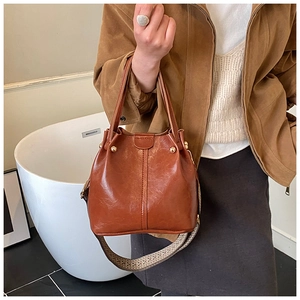Detailansicht der braunen Bucket Bag mit glänzendem Leder, Nieten und Web-Schultergurt