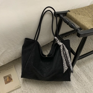 Detail of a black large-capacity tote bag with a decorative paisley scarf on a woven chair
