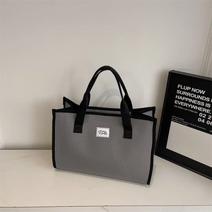 Detail of grey plaid tote bag with black piping and branding on a modern marble surface