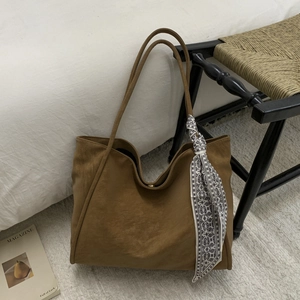Detailed close-up of brown faux leather tote bag with elegant silk scarf on white carpet