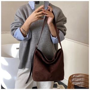 Detailed close-up of dark brown suede shoulder bag with wide strap and silver metal buckle