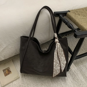 Detail of dark brown leather tote bag featuring a decorative paisley silk scarf handle