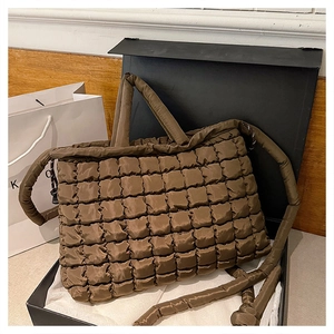 Detail of a brown quilted puffer tote bag with glossy texture and padded handle in a gift box