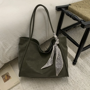 Detail of dark green large tote bag with silk scarf accessory and minimalist leather texture