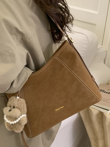 Sac bandoulière en daim marron avec surpiqûres blanches et charme en peluche porté par mannequin