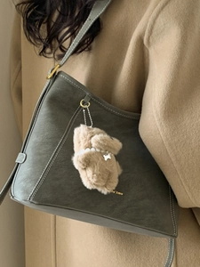 Sac seau chic en cuir gris-vert avec breloque ours porté sur un manteau en laine marron