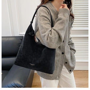 Detail of black suede tote bag with silver logo worn by model in a modern home setting