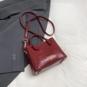 Dettaglio borsa a secchiello rossa con trama a coccodrillo, logo oro e tracolla regolabile