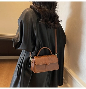 Brown leather crossbody bag with geometric flap detail and gold hardware on black coat