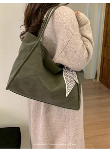 Detail of dark olive green tote bag with decorative scarf on model in minimalist interior