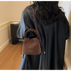 Close-up of brown bucket bag with woven handle and drawstring metal detail on a model
