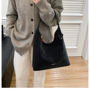 Close-up of large black suede hobo bag with white logo carried by a model