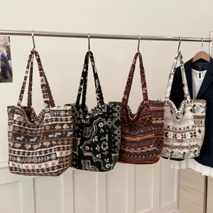 Detail view of four plush tote bags with ethnic jacquard patterns hanging on a metal rack