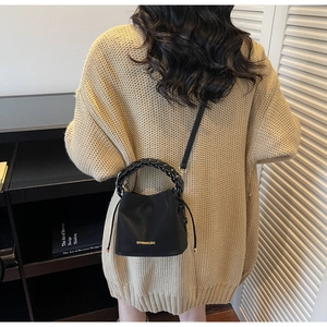 Detail of black leather bucket bag with woven handle and gold logo on knit sweater