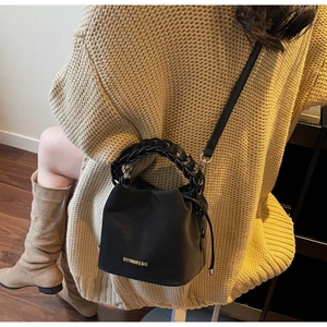 Detail view of a black bucket bag with a chunky chain handle and adjustable crossbody strap