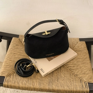 Sac à main noir mat avec boucle dorée sur un magazine et une chaise en rotin