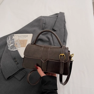 Detail view of retro brown crossbody bag with gold buckle on a stylish suit backdrop