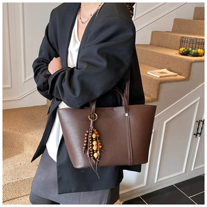 Detail of a dark brown leather tote bag featuring a retro beaded tassel and clean stitching