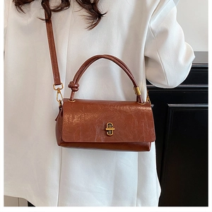 Detail of vintage brown leather handbag featuring a gold twist lock and a knotted top handle