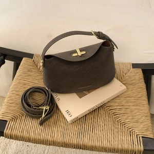 Détail d'un sac à main en cuir marron avec fermoir doré posé sur une chaise vintage