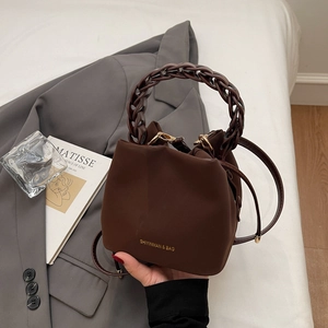 Detail of a brown matte bucket bag with gold lettering and woven chain handle