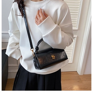 Black glossy leather handbag with twist lock and golden hardware worn by a model