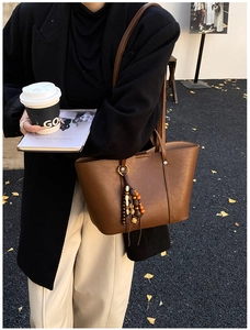 Close-up of brown leather tote bag with wooden bead tassel charm on street with autumn leaves