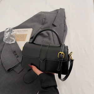 Detail of black leather handbag featuring vertical embossing and gold metal buckle
