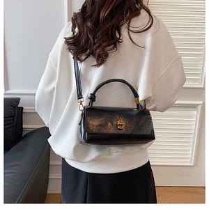 Detailed view of black leather handbag featuring gold twist lock and knotted top handle design