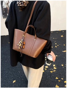 Brown tote bag with beaded tassel detail against a vintage autumn street background