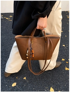 Detail of a brown leather tote bag with unique wood and ceramic bead tassel charms