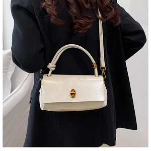 Polished white leather handbag with golden twist lock detail on elegant black suit