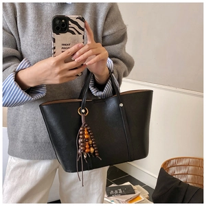 Detail of a large black leather tote bag featuring a decorative brown wooden bead tassel