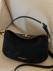 Sac à main minimaliste en cuir noir avec fermoir doré sur canapé, style décontracté