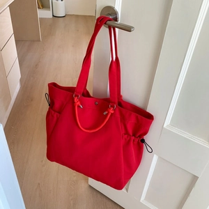 Close-up of red tote bag with drawstring toggles hanging on a white door handle