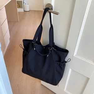 Detail of black large-capacity tote bag with adjustable side drawstrings on a white door