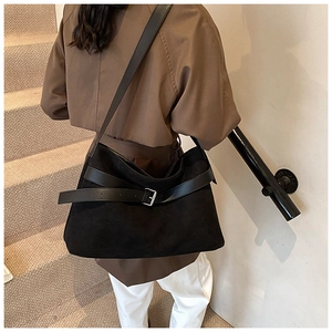 Detail view of black suede tote bag with silver buckle strap shown on model's shoulder