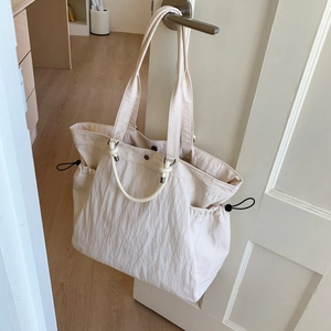 Detail of off-white oversized tote bag with decorative rope accents hanging on a door