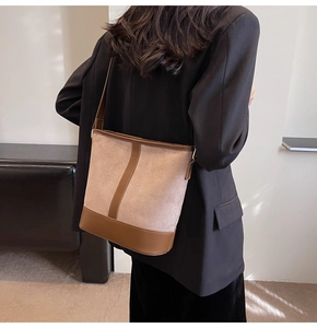 Detail of a brown and beige suede bucket bag shown worn as a crossbody on a model