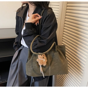Detailed close-up of olive green canvas tote bag with white stitching and bear charm