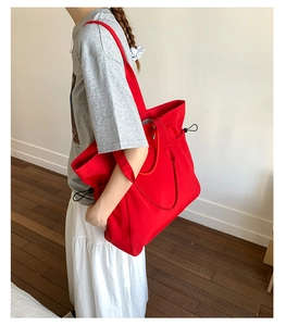 Detail of red large capacity nylon tote bag with drawstring closure and wide shoulder strap