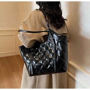 Detail of black quilted tote bag with glossy finish and silver metal ring accents