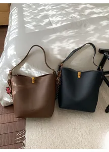 Détail de sacs seaux en cuir grainé marron et noir avec ferrures dorées sur lit blanc