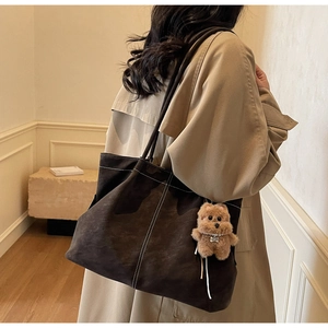 Detail of dark matte tote bag with contrast stitching and bear charm on beige trench coat