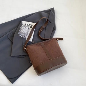Detail view of brown matte suede bucket bag with leather accents on a gray suit