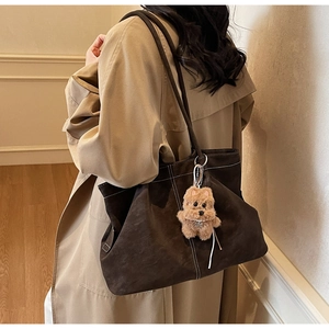 Detail of a large brown tote bag with white stitching and plush dog charm accessory