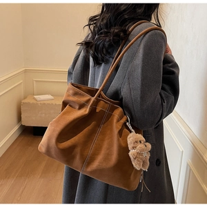 Detail of caramel suede tote bag with white contrast stitching and plush bear charm